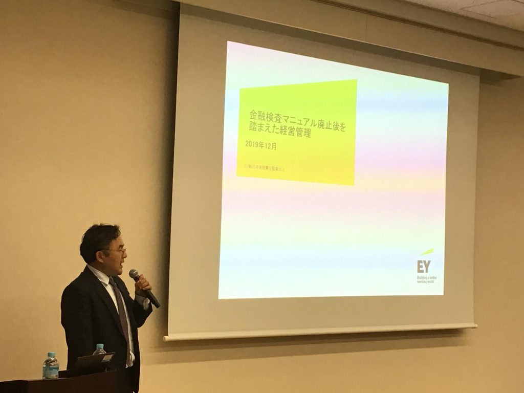 EY新日本有限責任監査法人の神崎有吾氏がスクリーンの前でプレゼンテーションを行っている場面の写真